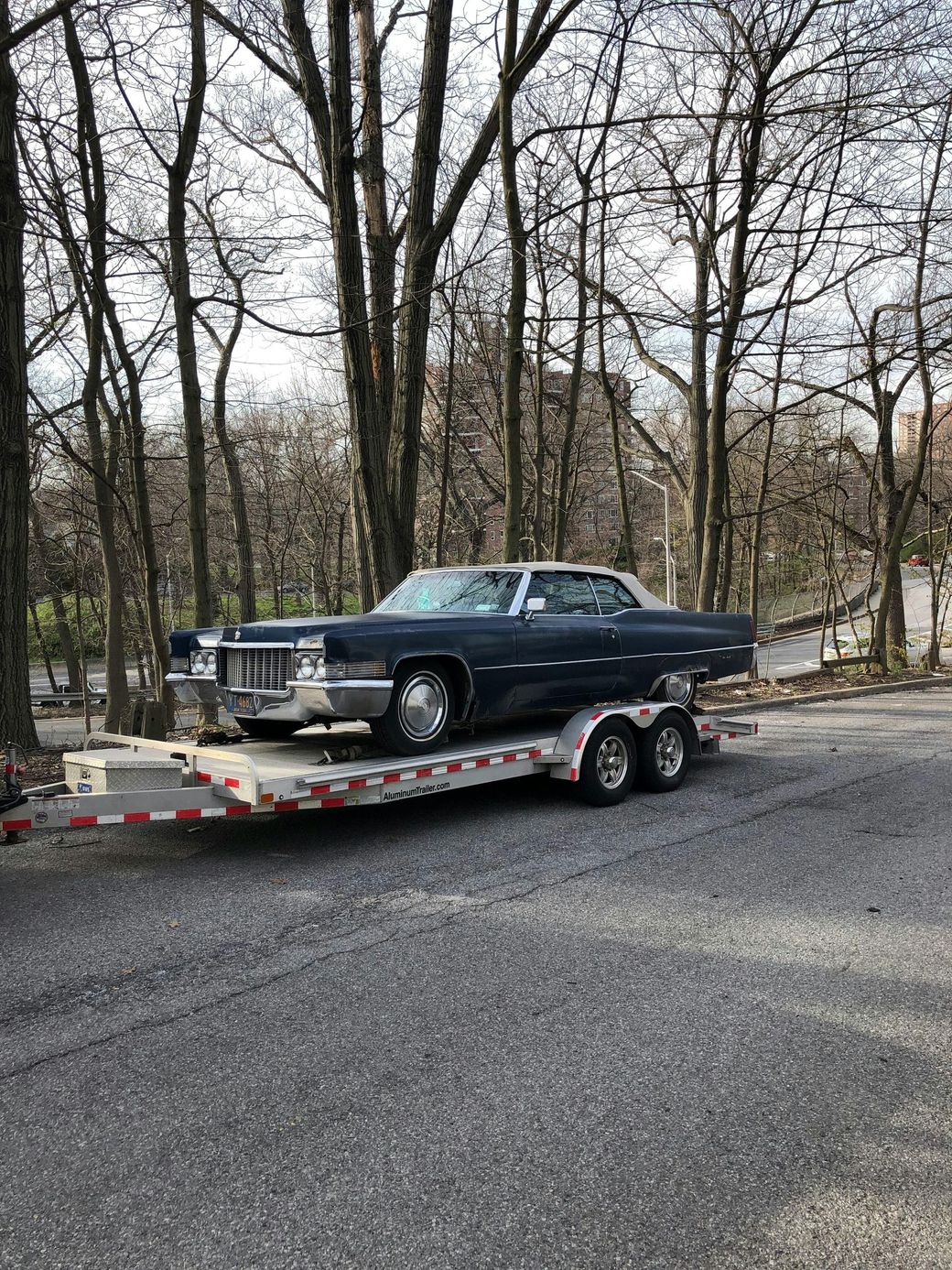 A black car is sitting on top of a trailer in a parking lot.