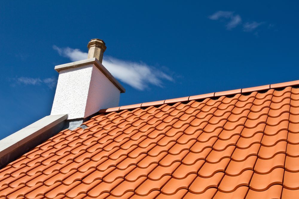 A Chimney on Top of a Tiled Roof With a Blue Sky in the Background — Timms Roofing In Shellharbour, NSW