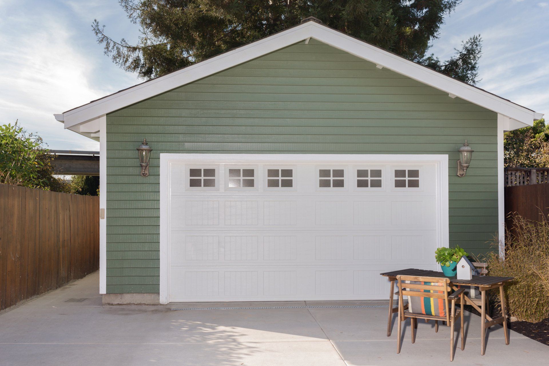 A green garage with a white door and a table and chairs in front of it.