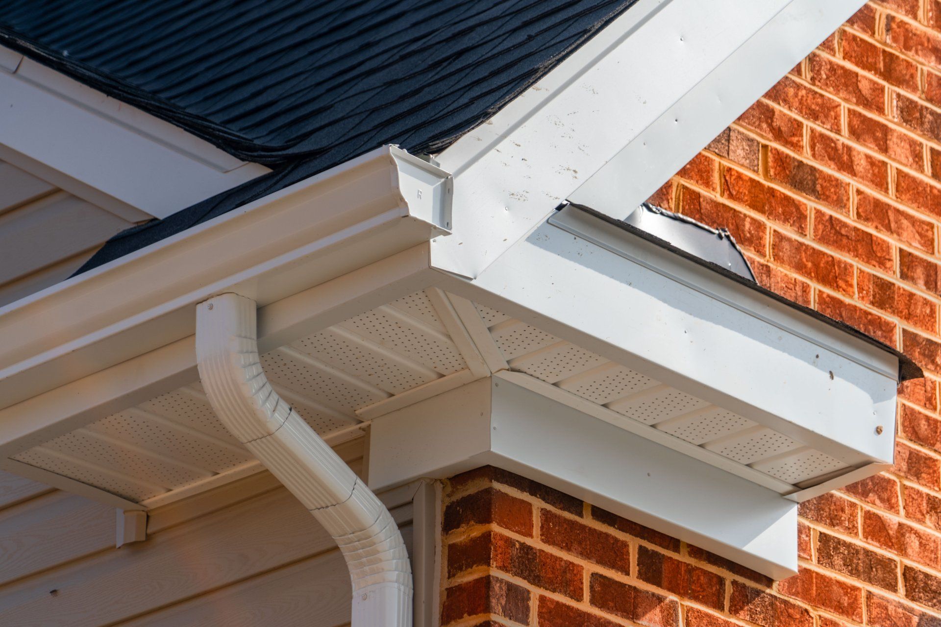 A brick house with a white gutter and a black roof.