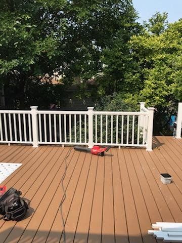 A wooden deck with a white railing and trees in the background.