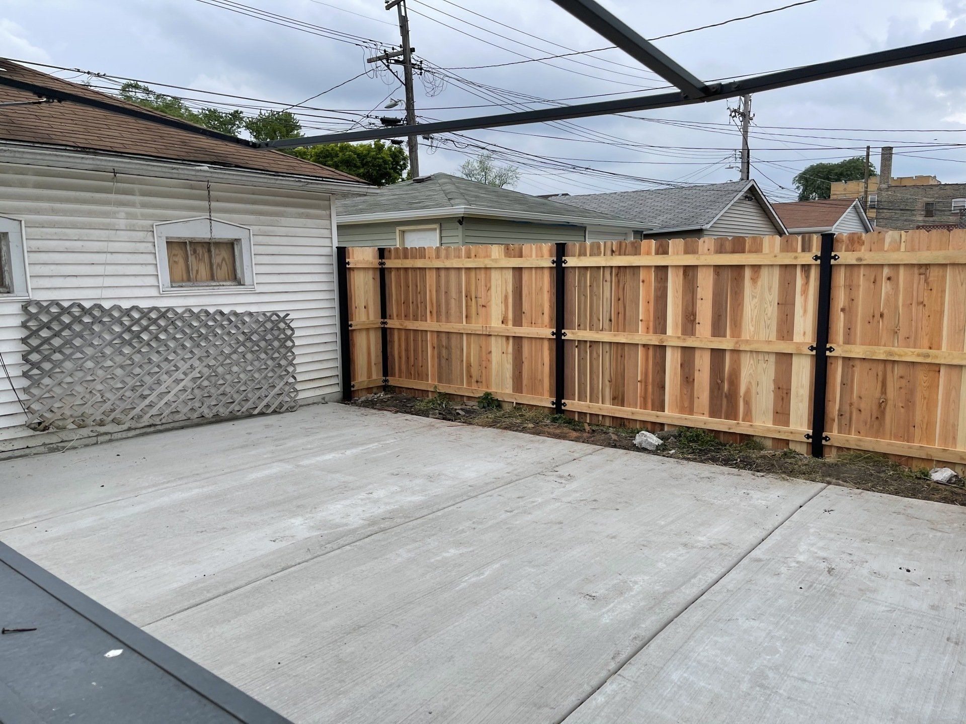 A wooden fence surrounds a concrete driveway in front of a house.