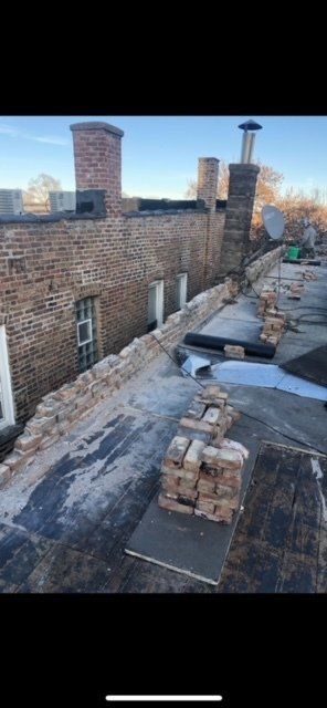 A brick building with chimneys on the roof and a stack of bricks on the roof.