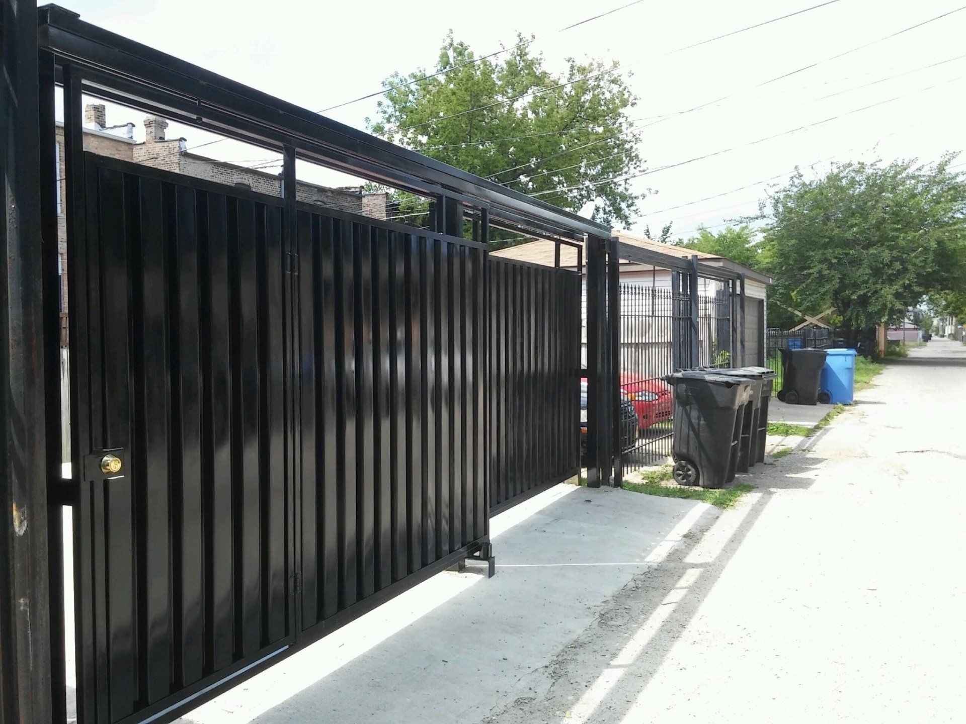 A black fence is sitting on the side of a street next to a trash can.