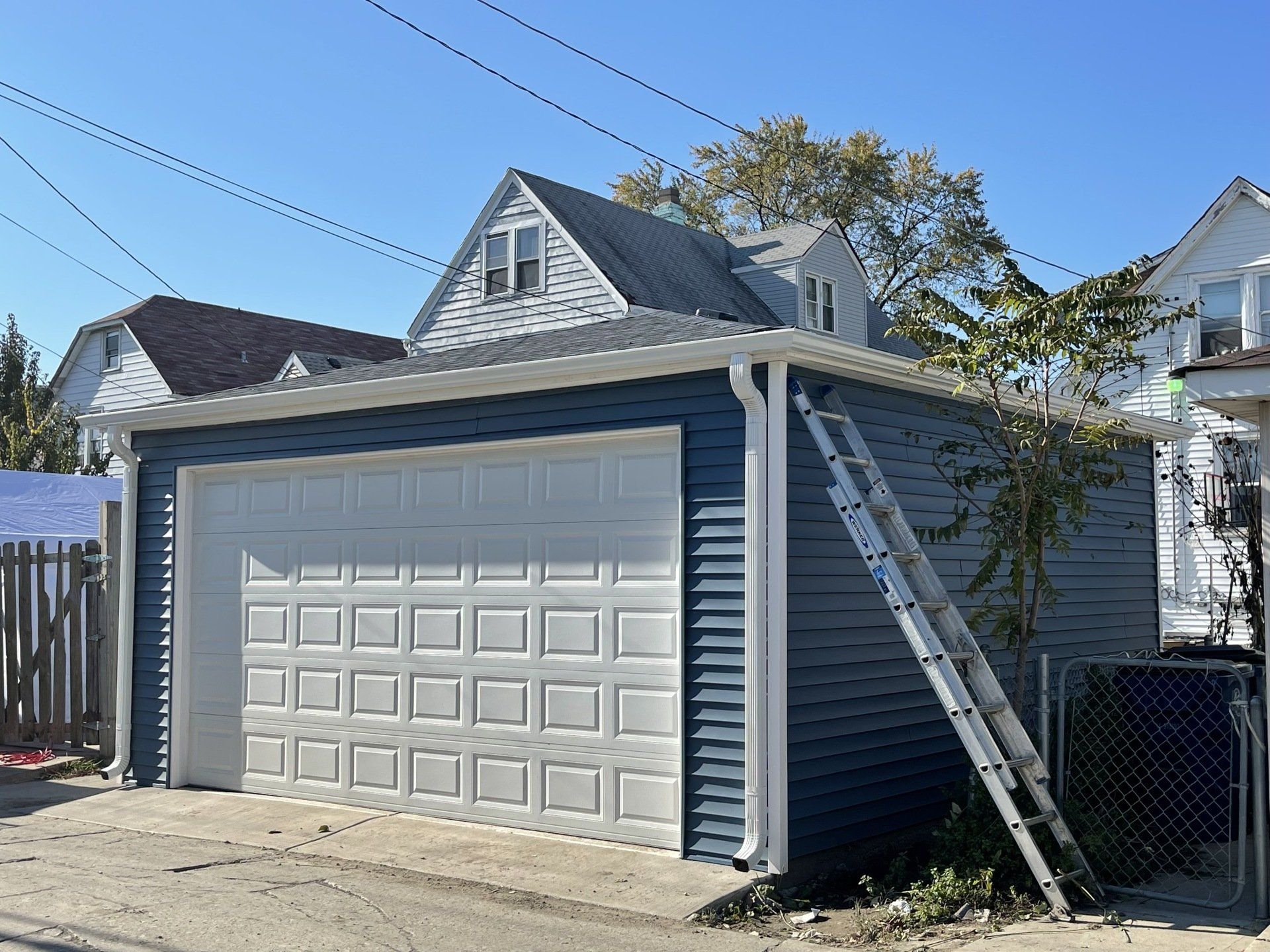 A blue and white garage with a ladder leaning against it.