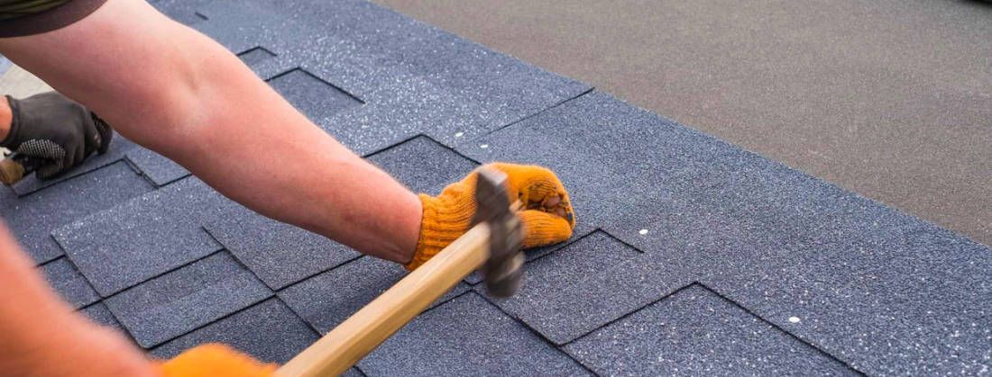 A person is hammering a nail into a roof with a hammer.