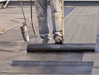 A man is rolling a roll of roofing material on a roof.