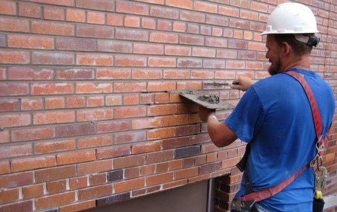 A man wearing a hard hat is working on a brick wall.