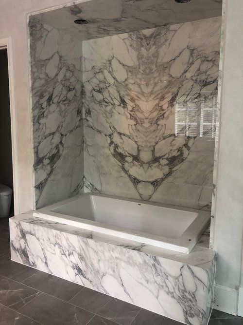 A bathtub is surrounded by marble in a bathroom