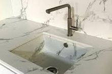 A kitchen sink with a faucet on a marble counter top
