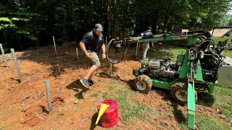 A man is digging a hole in the ground next to a green tractor.
