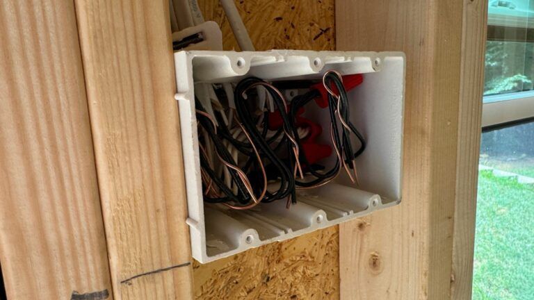 A white electrical box is sitting on a wooden wall.