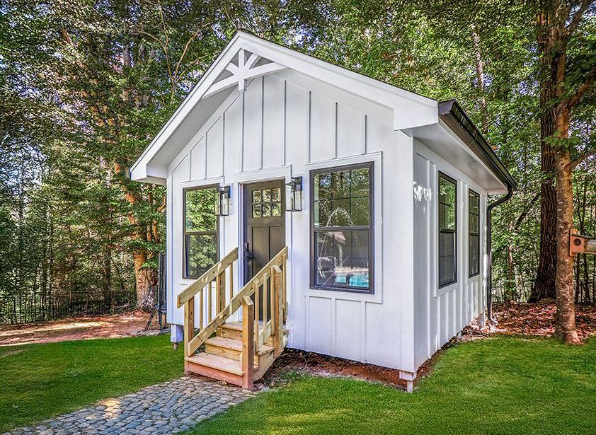 A small white house with stairs leading up to it is sitting on top of a lush green lawn.