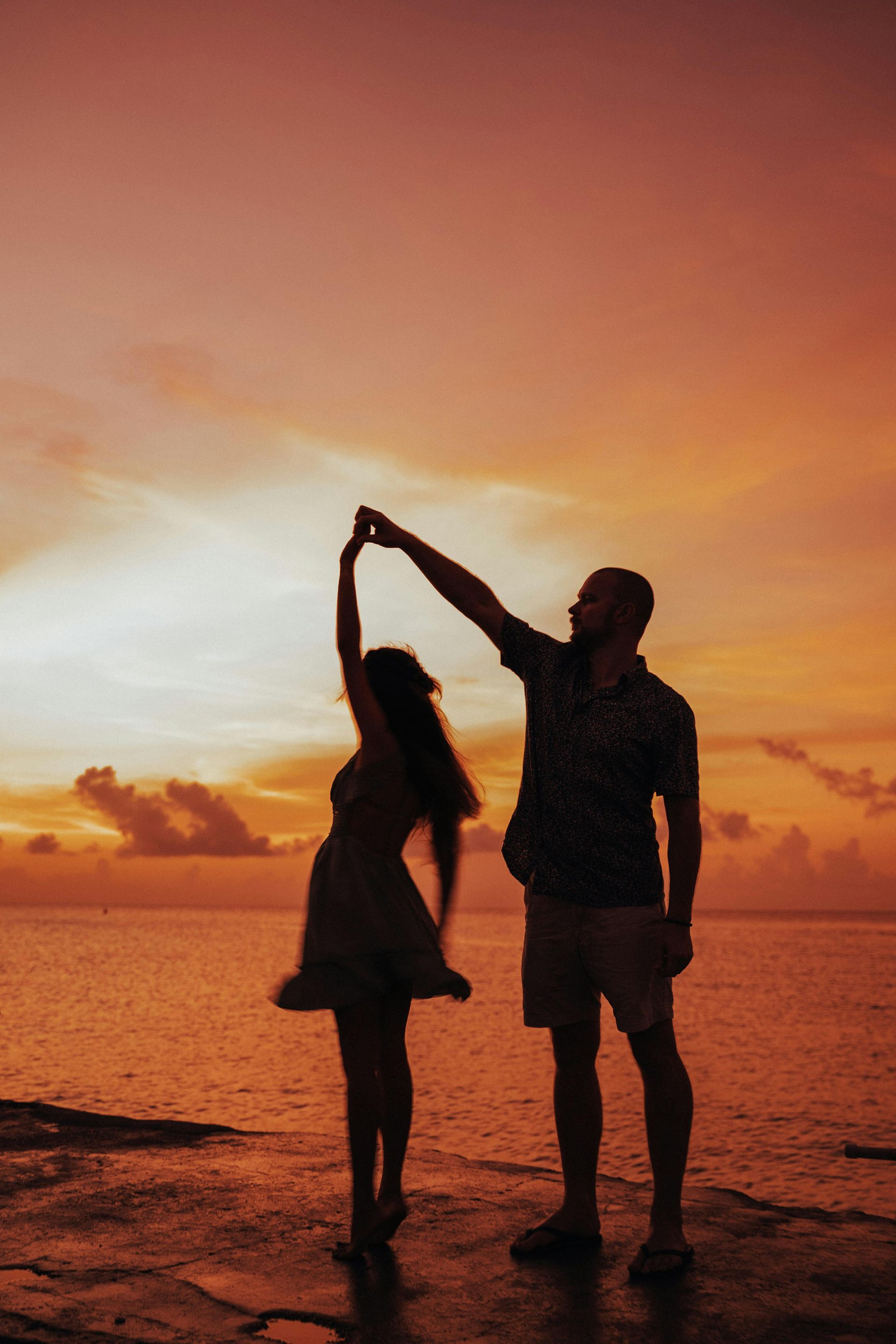 A man and a woman are dancing on the beach at sunset.