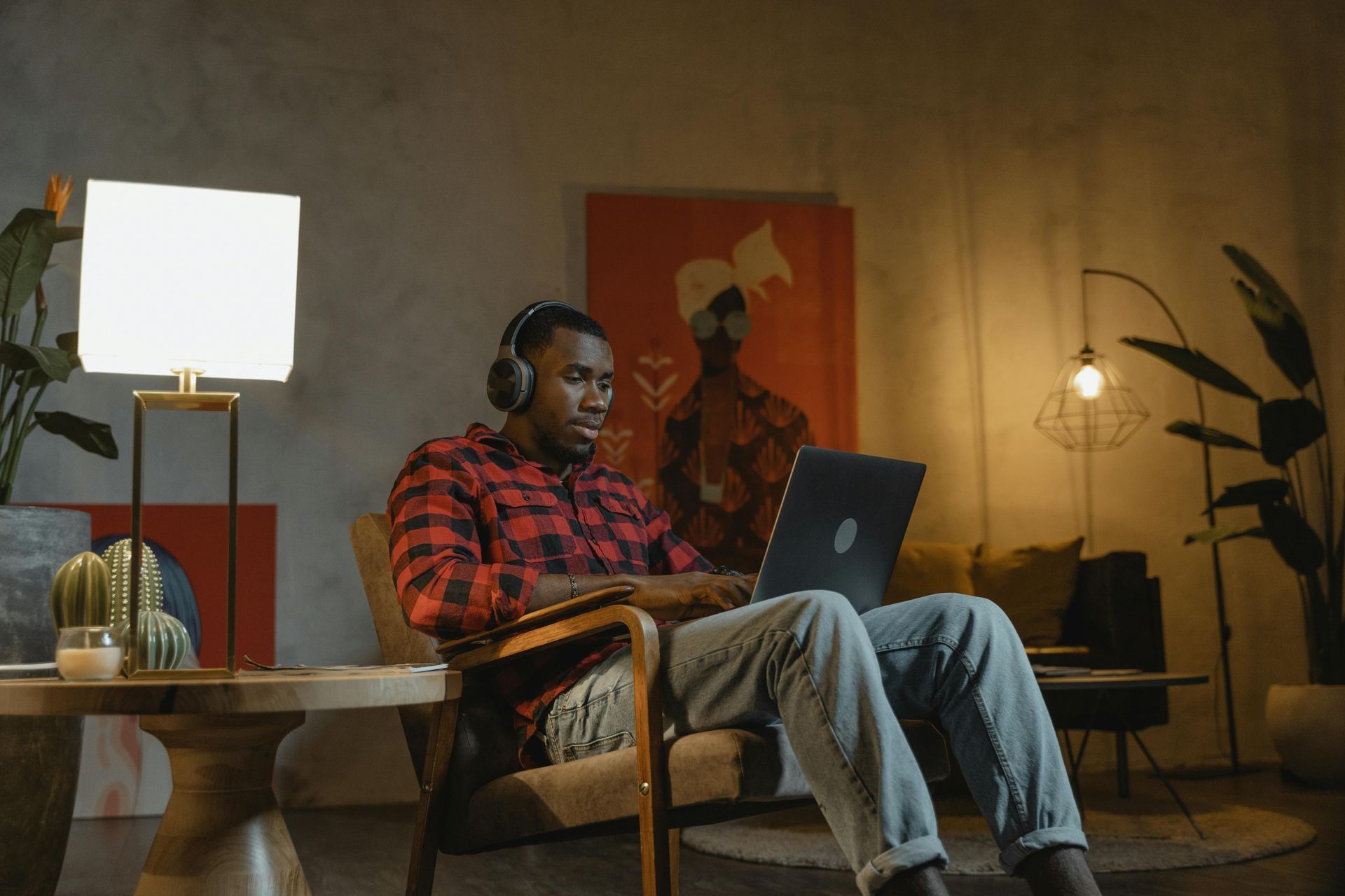A man wearing headphones is sitting in a chair using a laptop computer.