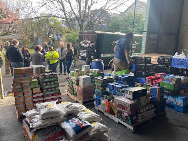 Seattle community food bank event showing volunteers and large stacks of non-perishable food donations for local families.