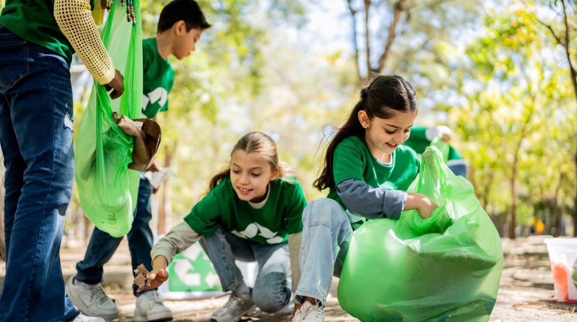 Young volunteers in 'recycle' logo shirts actively participating in an outdoor environmental clean-up, collecting trash in green bags in a sunny Seattle park.