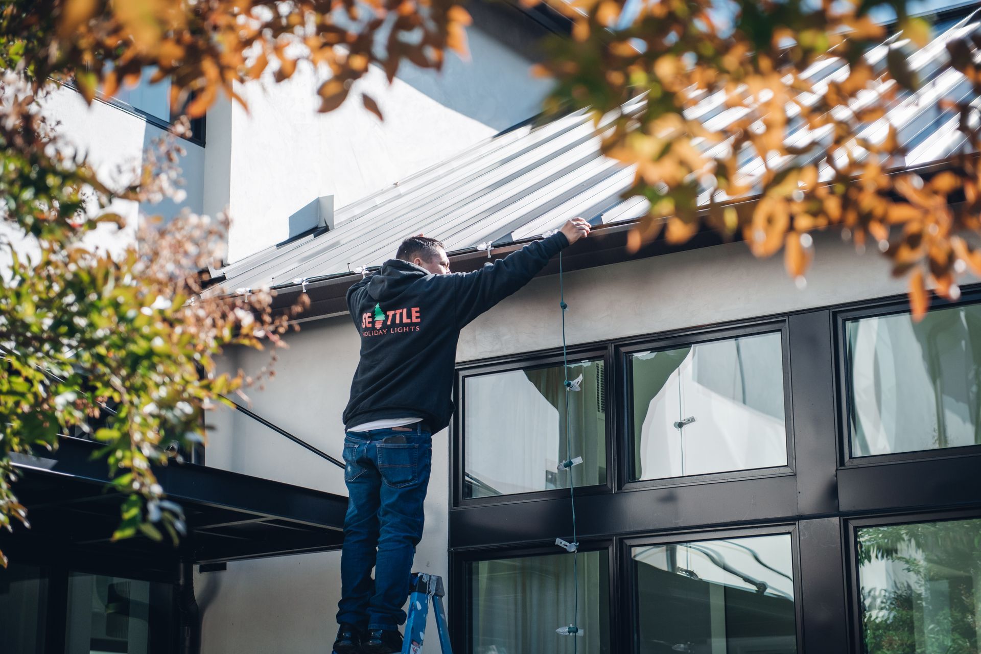 A man is standing on a ladder working on the roof of a building.
