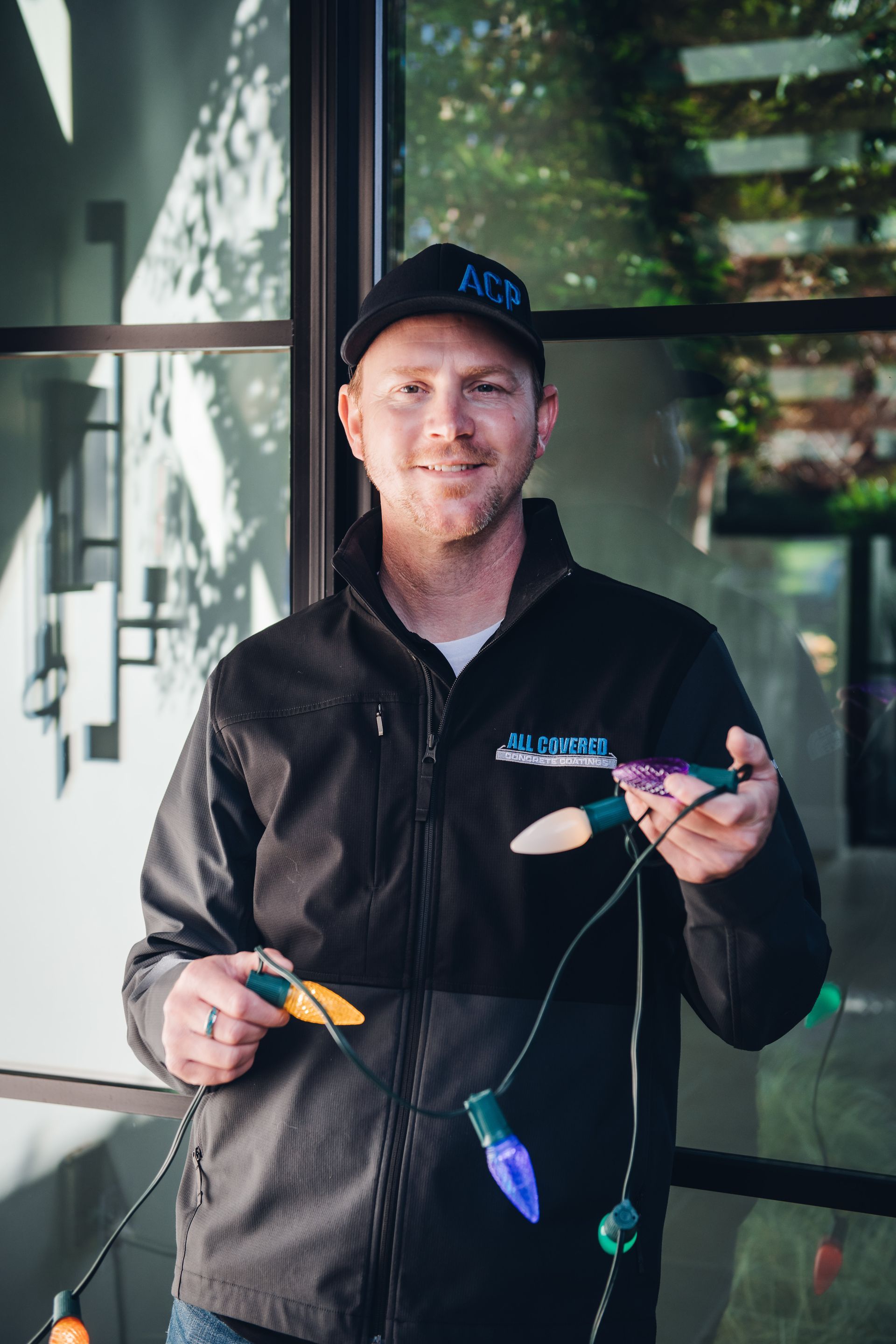 A man in a black jacket is holding a string of christmas lights.