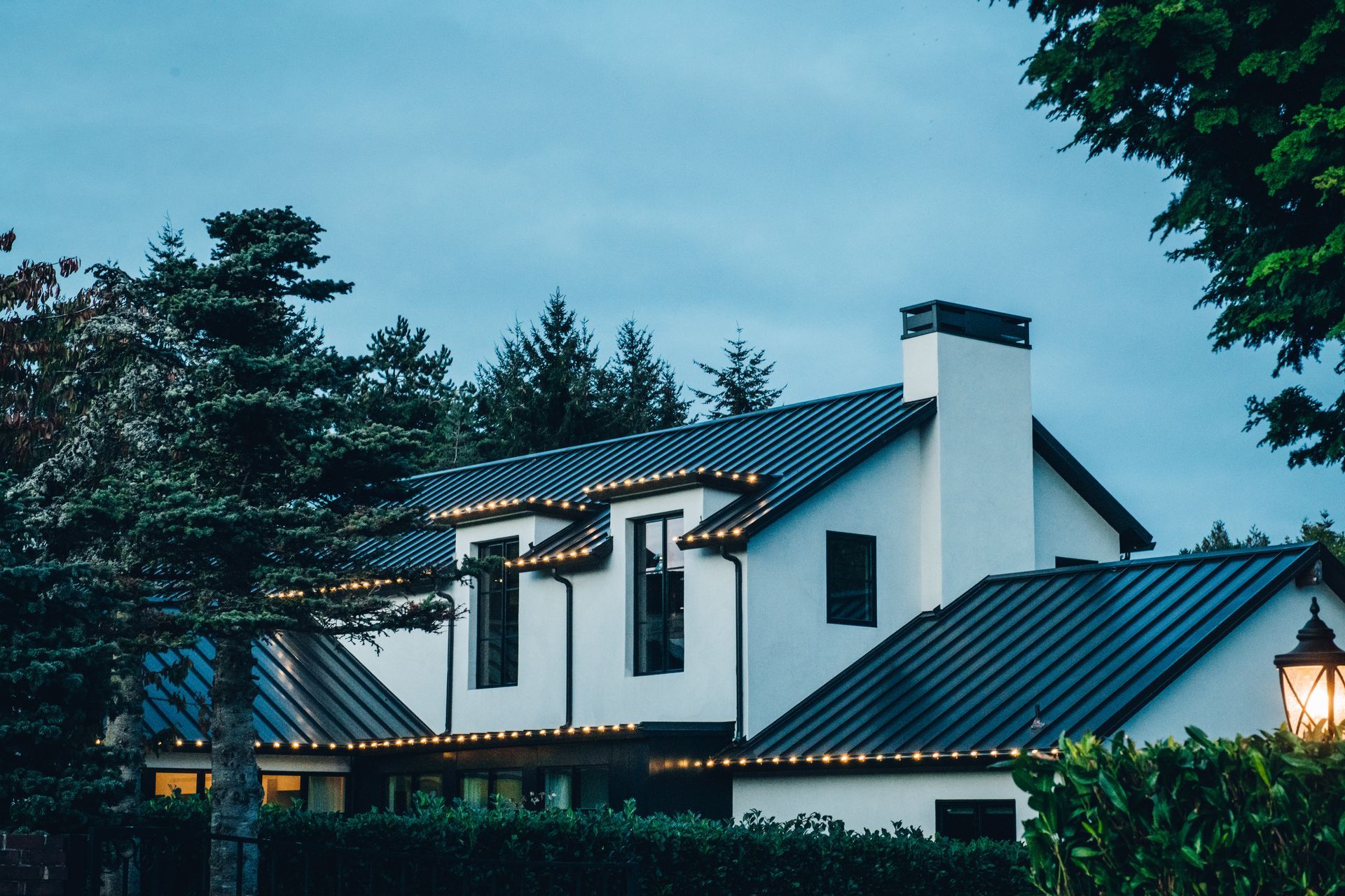 A white house with a black roof and christmas lights on it