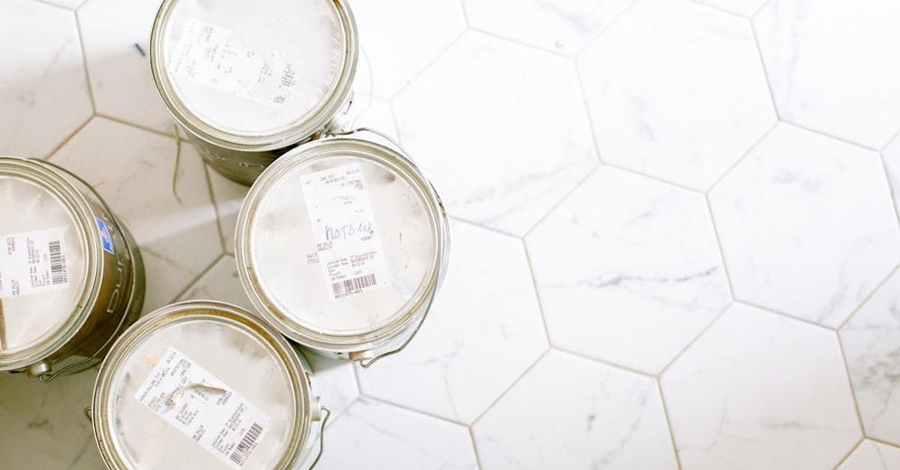 Four buckets of paint are stacked on top of each other on a tiled floor.