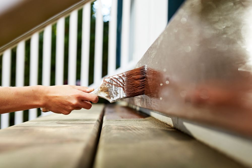 A person is painting a wooden deck with a brush.