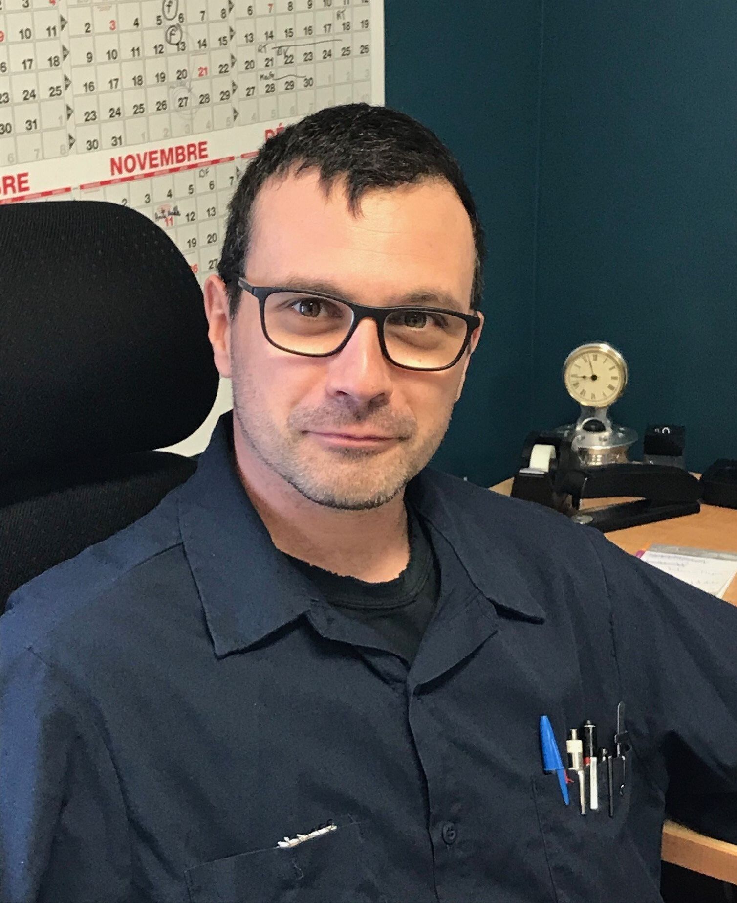 Un homme portant des lunettes est assis à un bureau devant un calendrier.