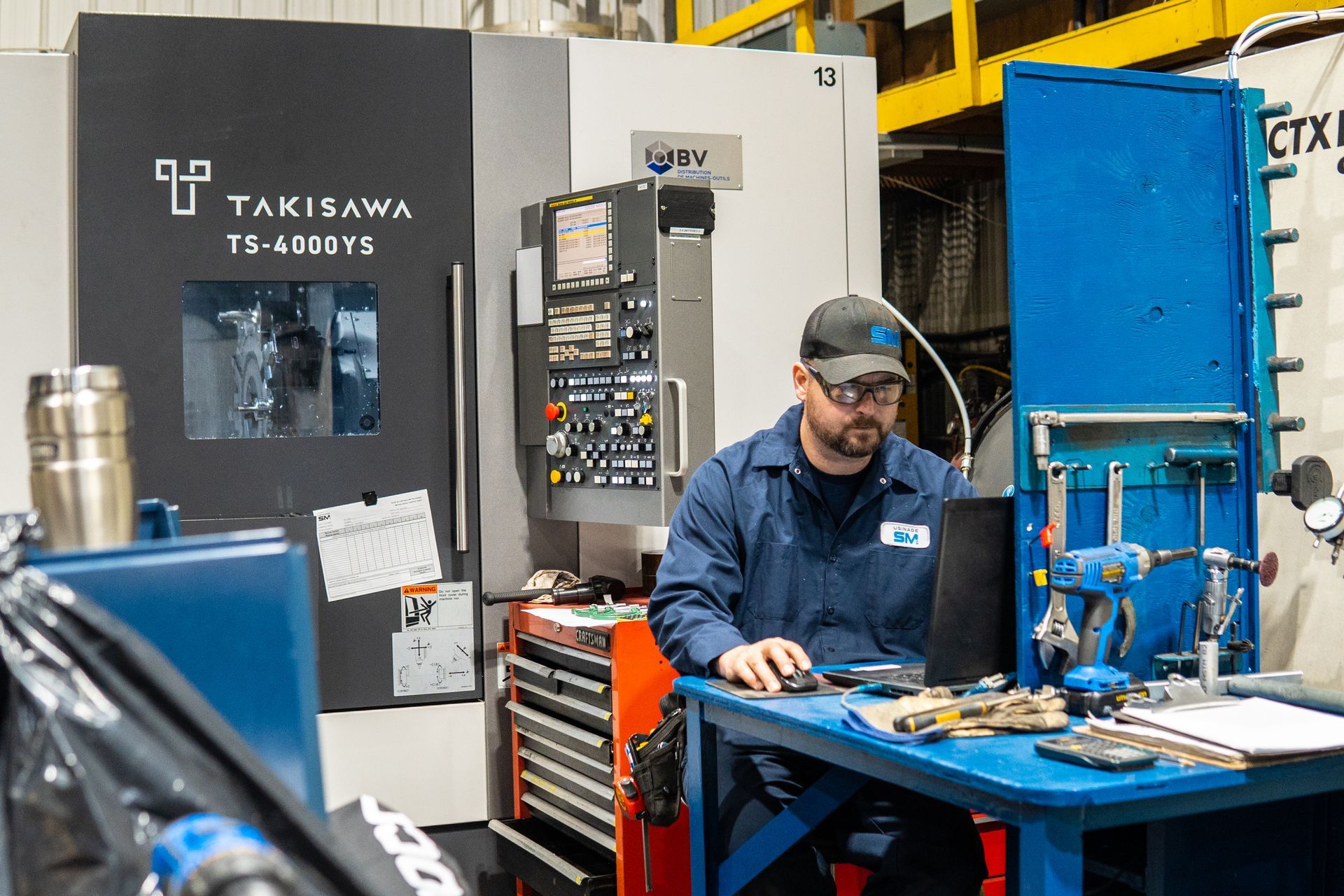 Un homme est assis à un bureau devant un ordinateur dans une usine.