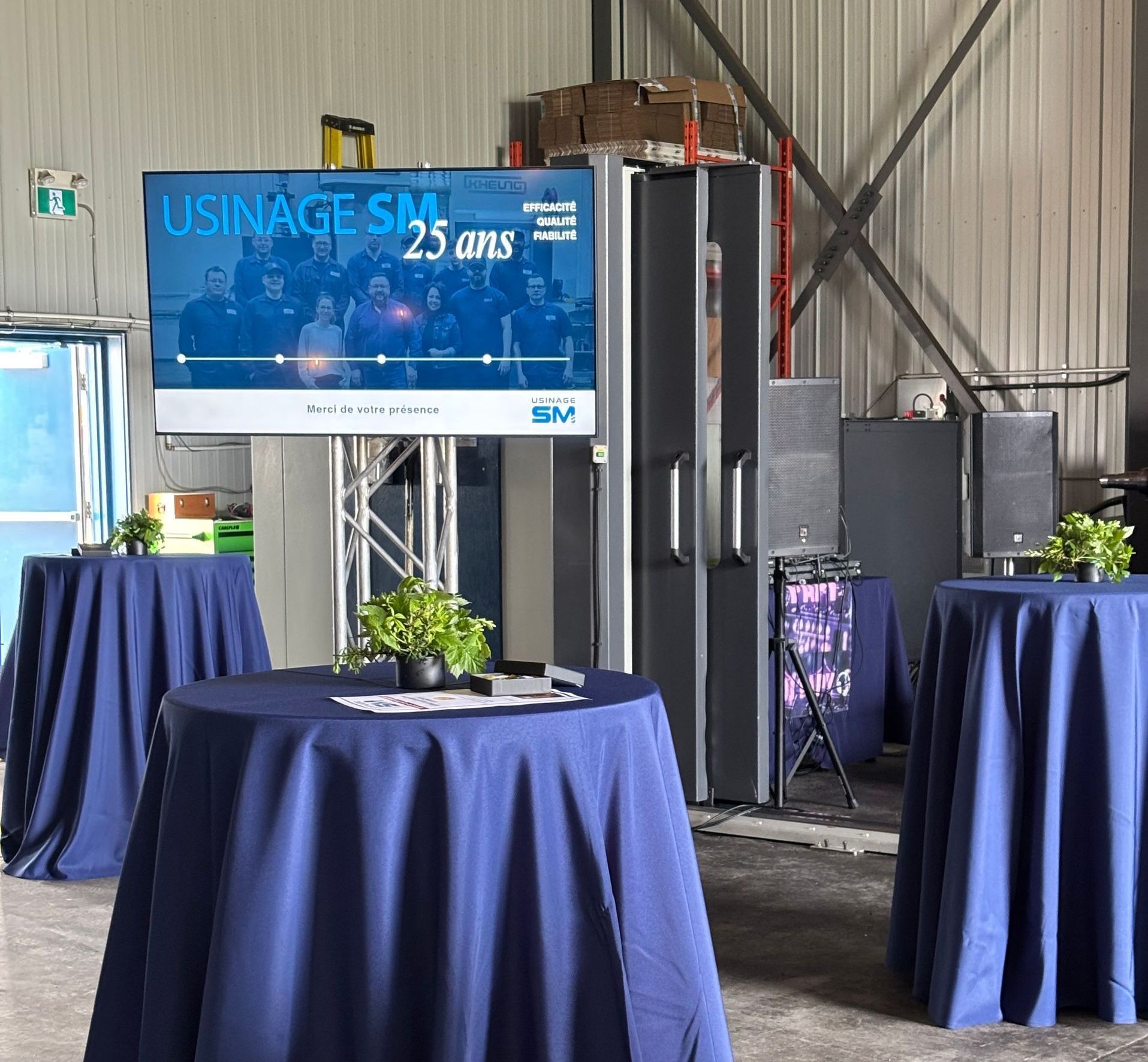 Une table avec une nappe bleue est devant un écran sur lequel est écrit usine sm 25 ans