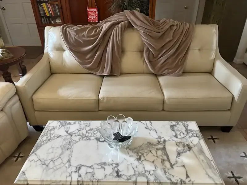 Cream sofa with draped taupe throw in a living room, behind a marble coffee table with a glass bowl centerpiece.