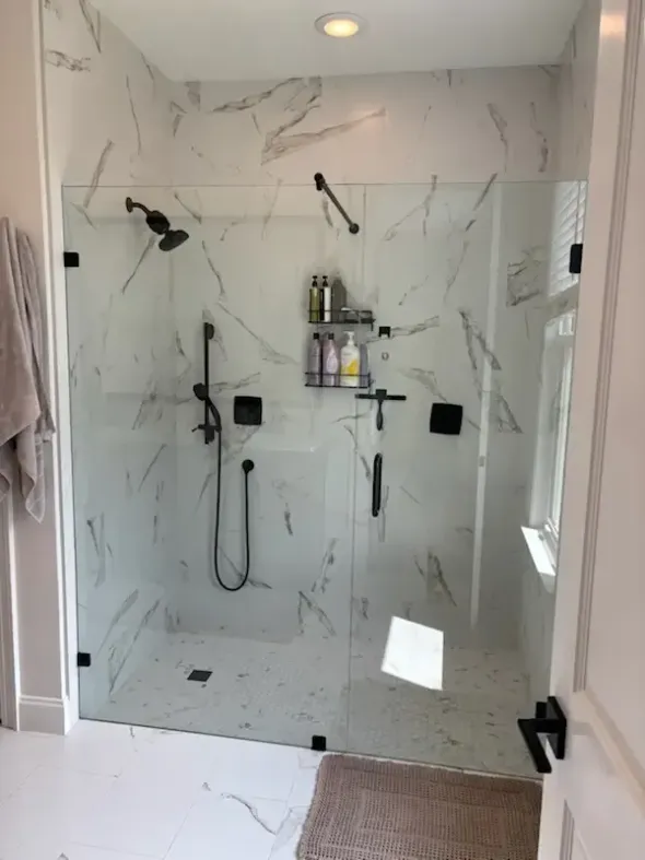 Modern marble-tiled walk-in shower with black fixtures, glass door, and built-in shelf undertile lights