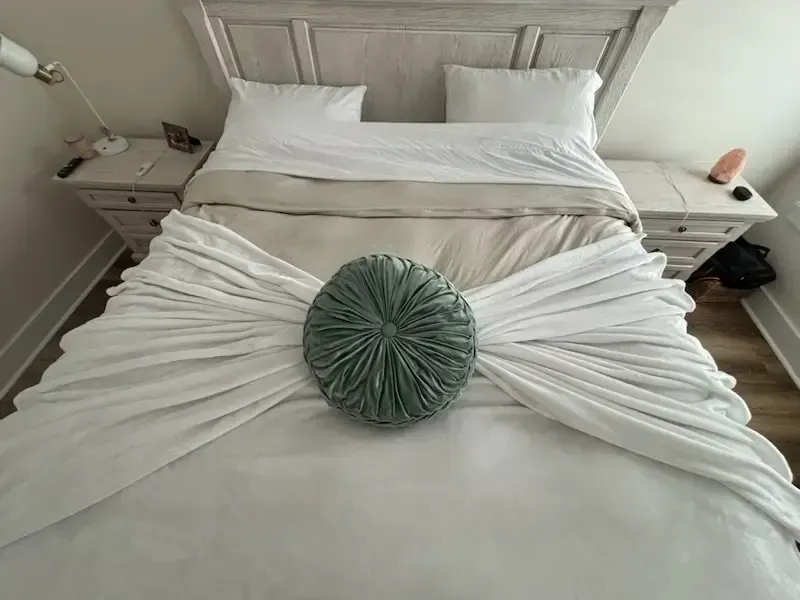 Neatly made bed with white bedding and a green round pillow at the center