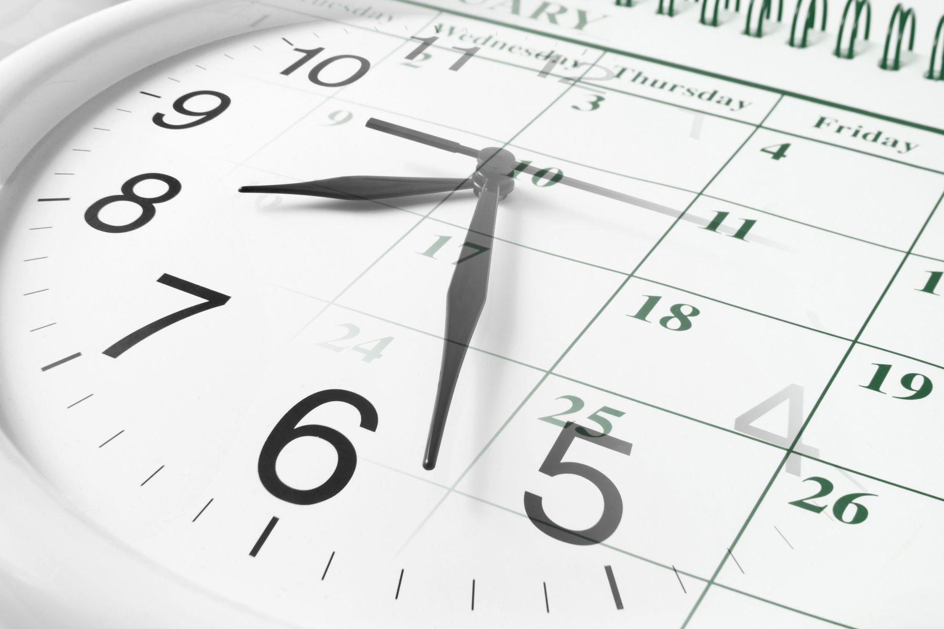 Close-up of a white clock over a calendar page, showing a scheduled date and time.
