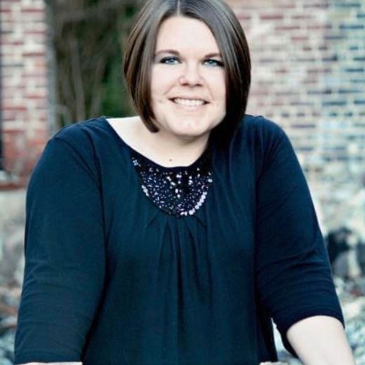 Woman with brown hair smiling in front of a brick wall, wearing a black top.