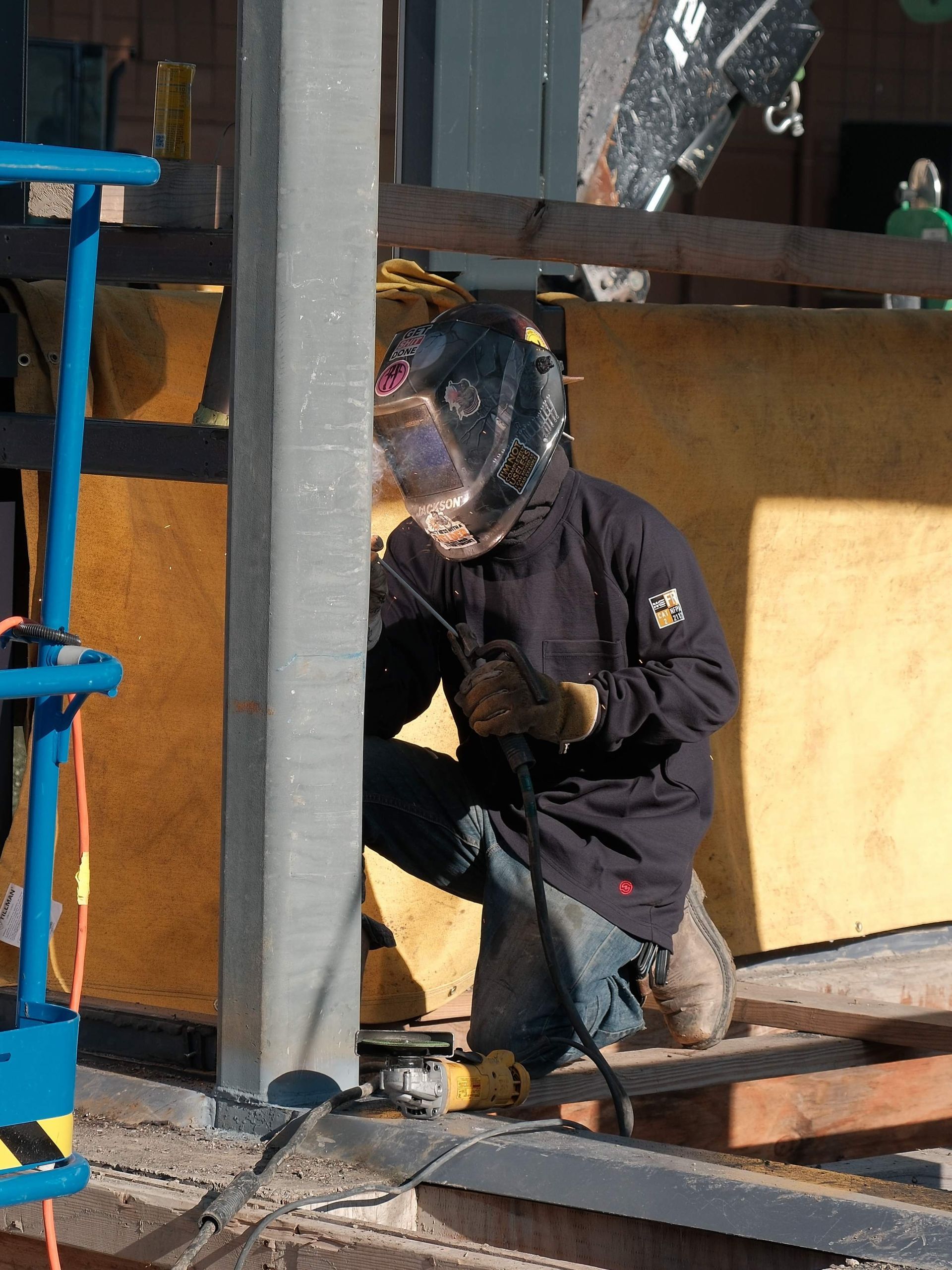 A man wearing a welding helmet is working on a metal structure