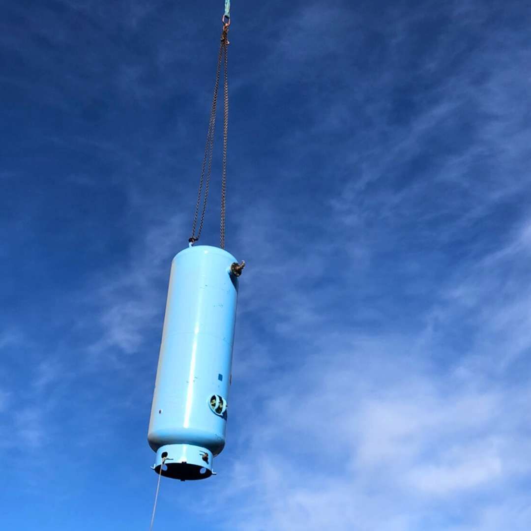 a large blue cylinder is being lifted by a crane against a blue sky .