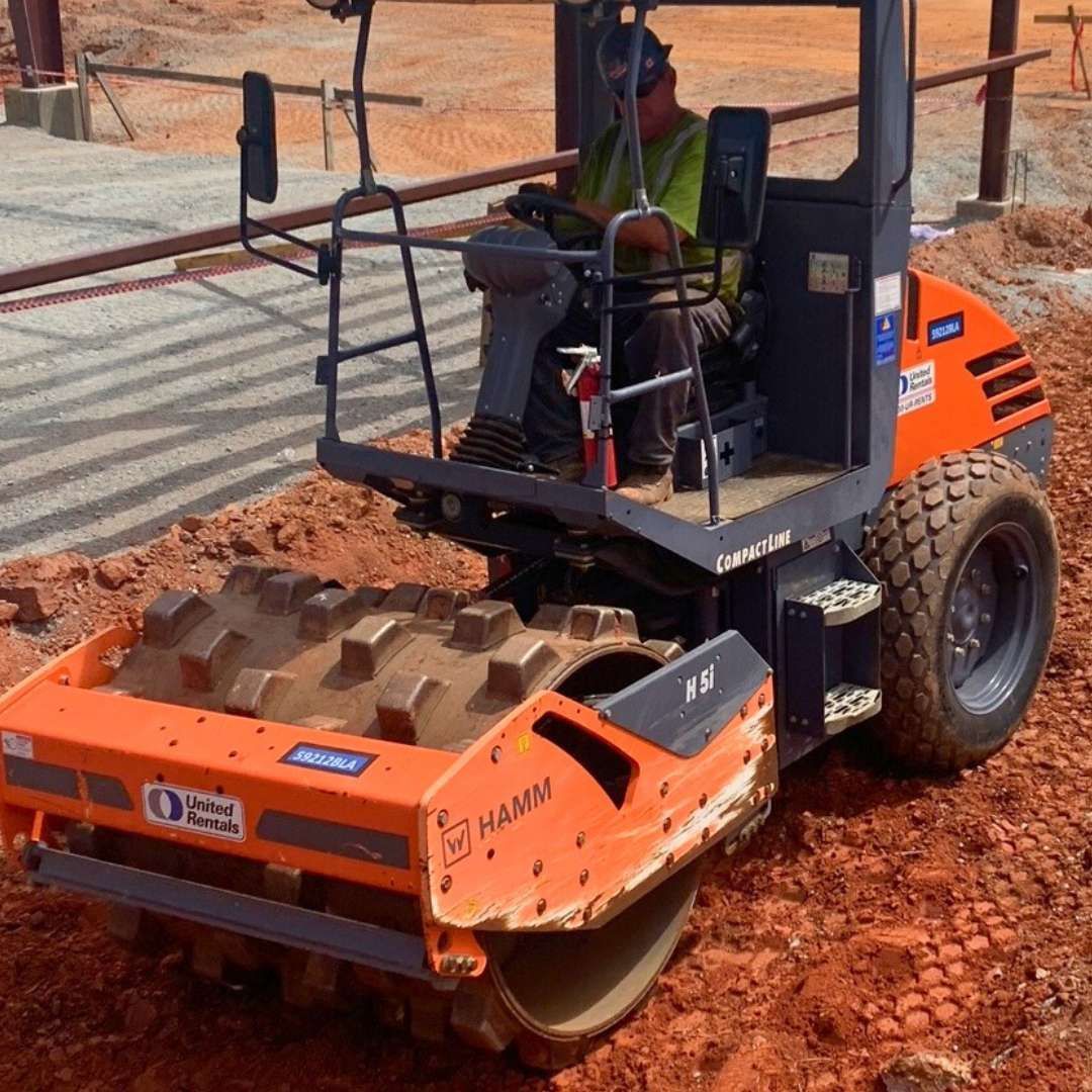 a man is driving a hamm roller on a dirt road