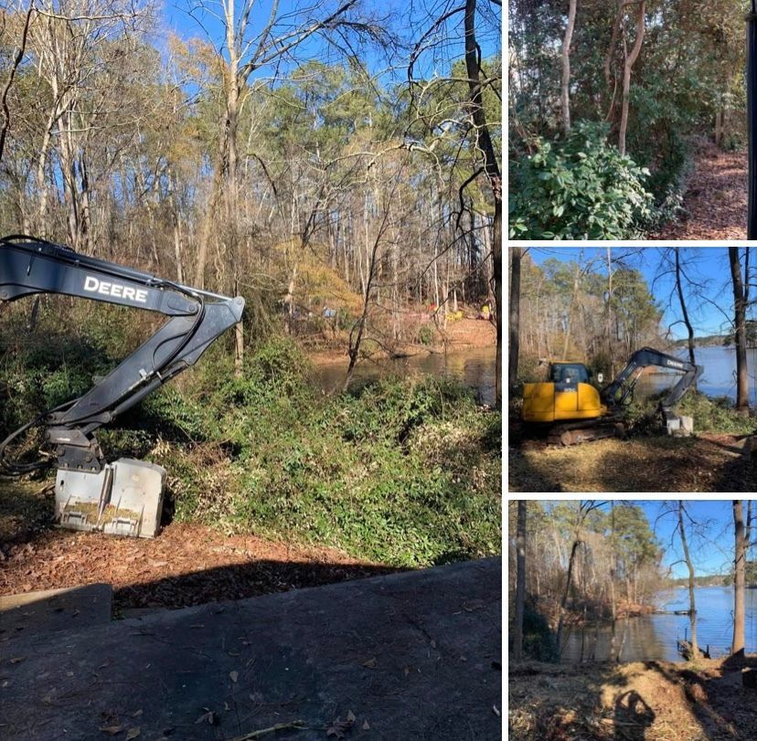 A John Deere excavator clears vegetation near a lakeshore on a sunny day.