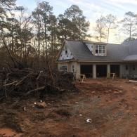 A large pile of brush and debris sits in front of a house under construction with a gray roof and light-colored siding.