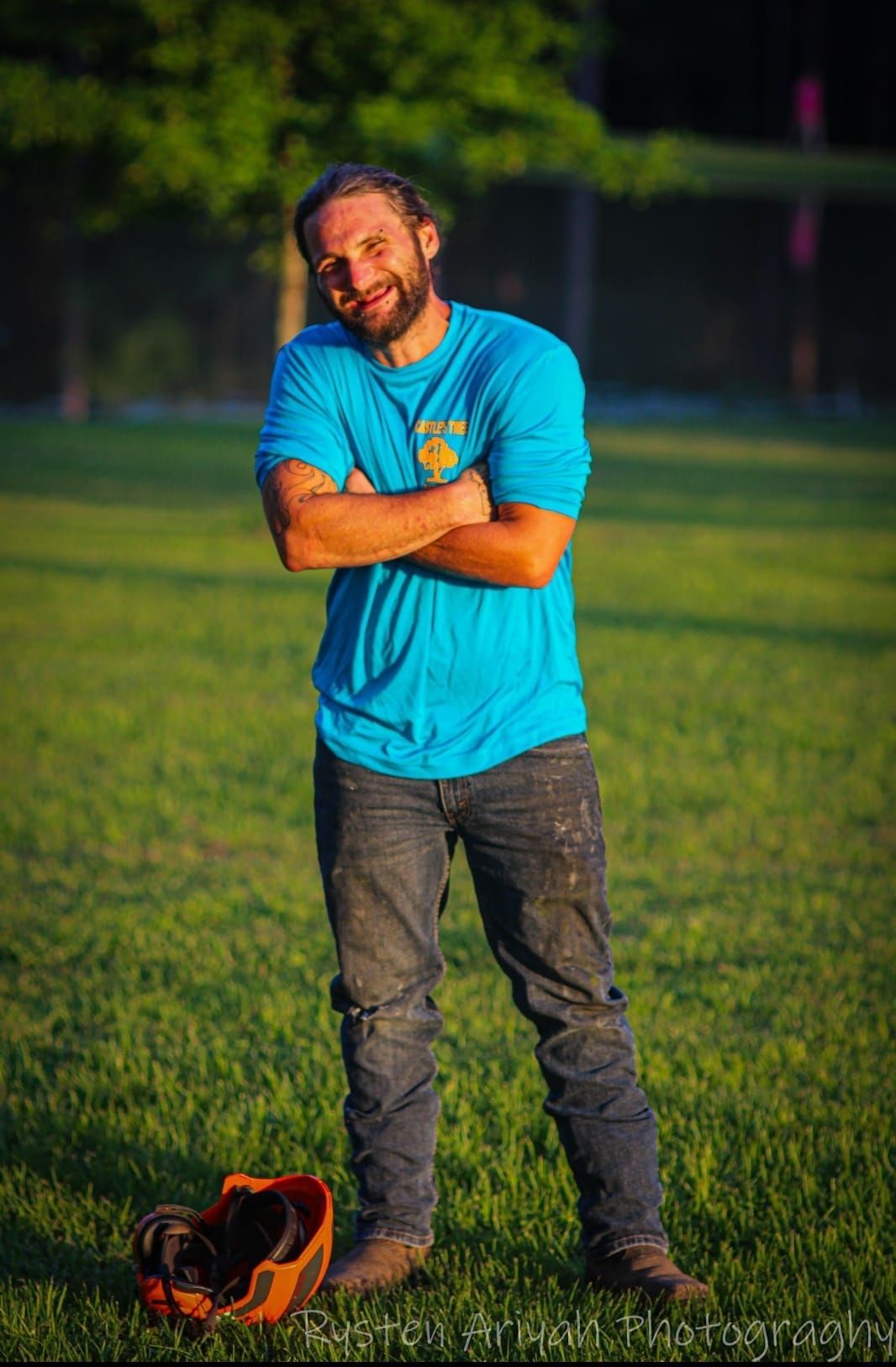 A man in a blue shirt is standing in a field with his arms crossed.