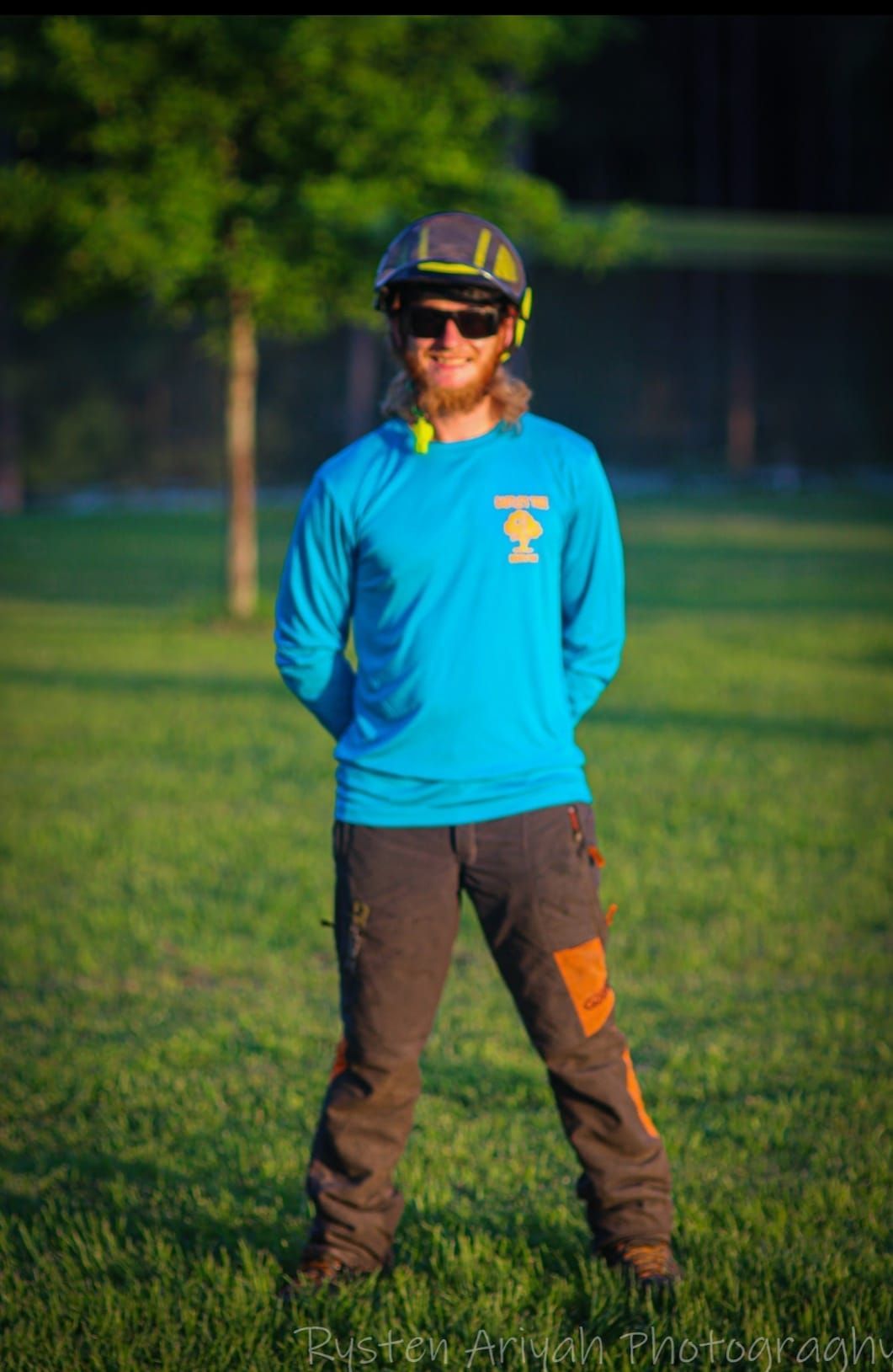 A man wearing a blue shirt and a helmet is standing in the grass.