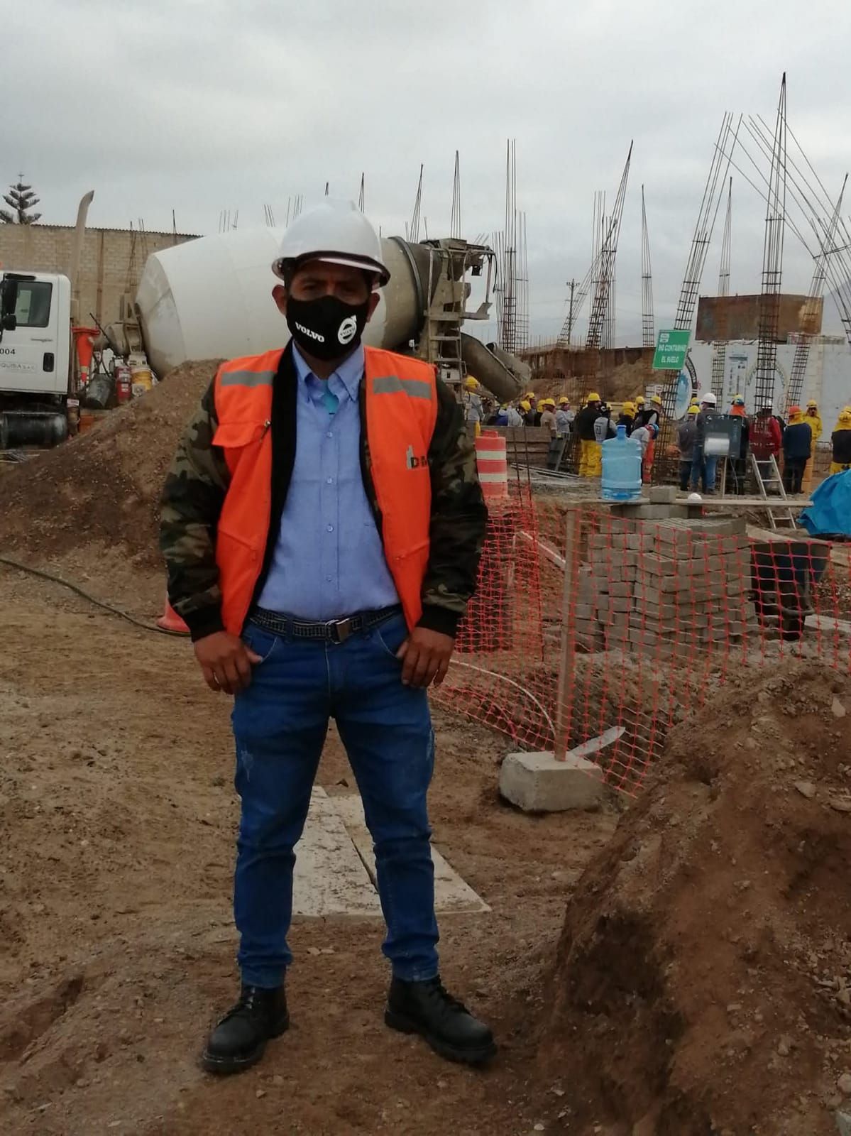 Trabajador de la construcción con casco, chaleco de seguridad y máscara, de pie en un sitio de construcción.
