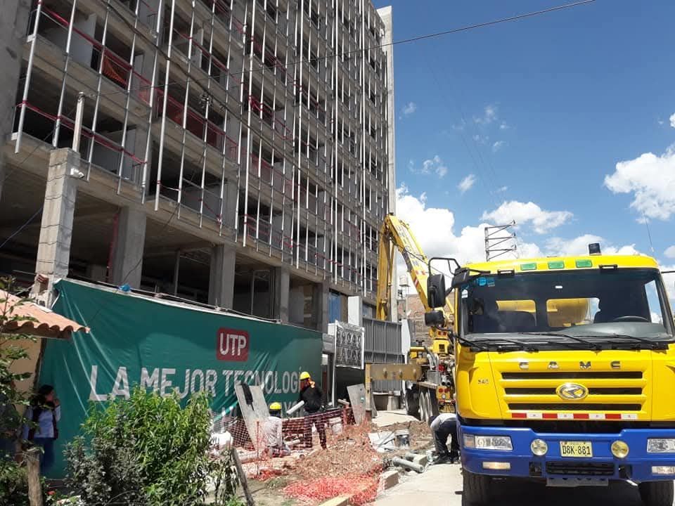 Sitio de construcción con un edificio alto en construcción, un camión amarillo y trabajadores en un día soleado.