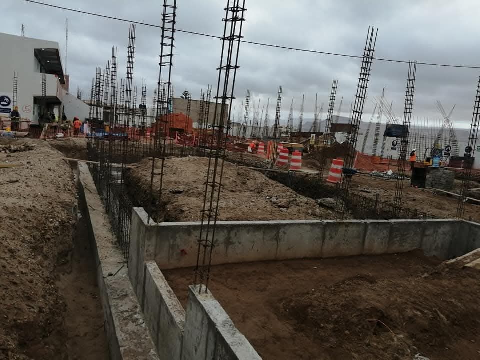 Sitio de construcción con cimientos de hormigón, varillas de refuerzo y conos de tráfico de color naranja.