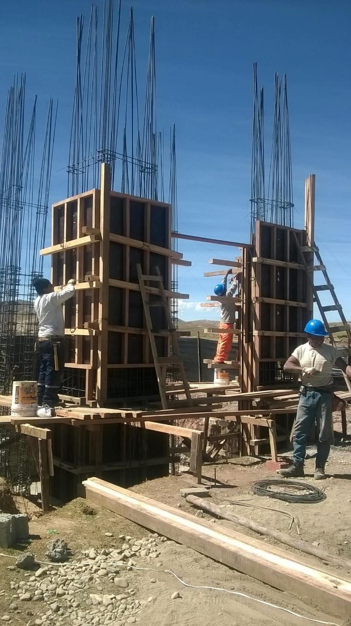 Obreros de la construcción construyen pilares de hormigón. Encofrados de madera, varillas de acero y cielo azul.
