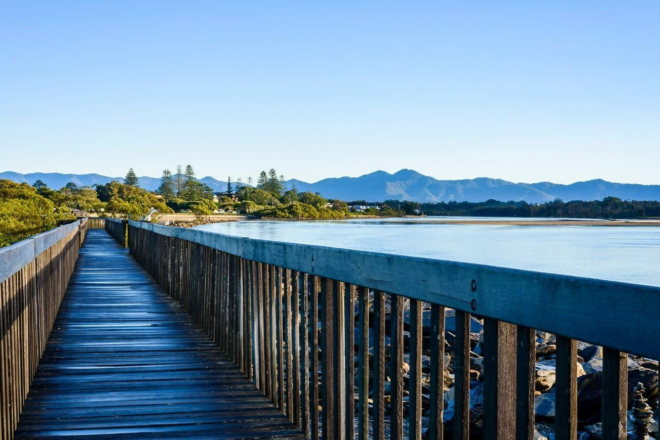 A Wooden Walkway Leading to A Lake with Mountains — All Round Ground Maintenance in Urunga, NSW