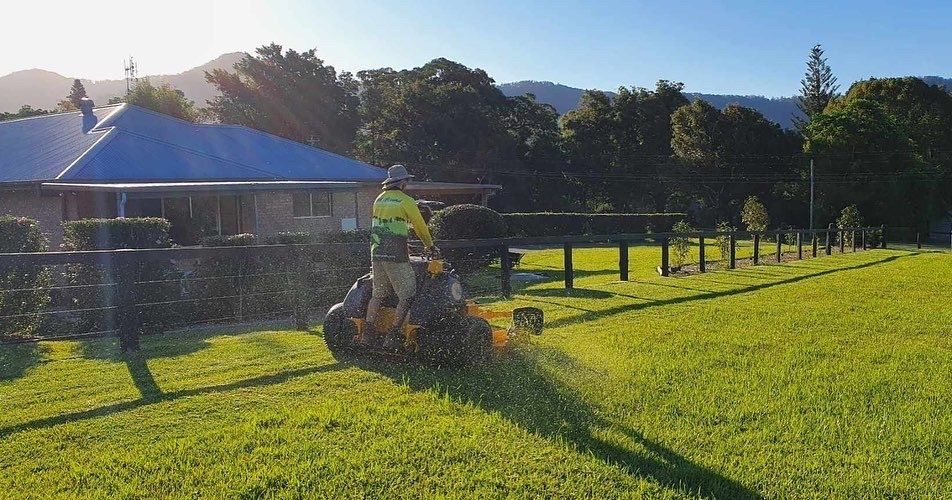A Man Is Riding a Lawn Mower on A Lush Green Field — All Round Ground Maintenance in Woolgoolga, NSW