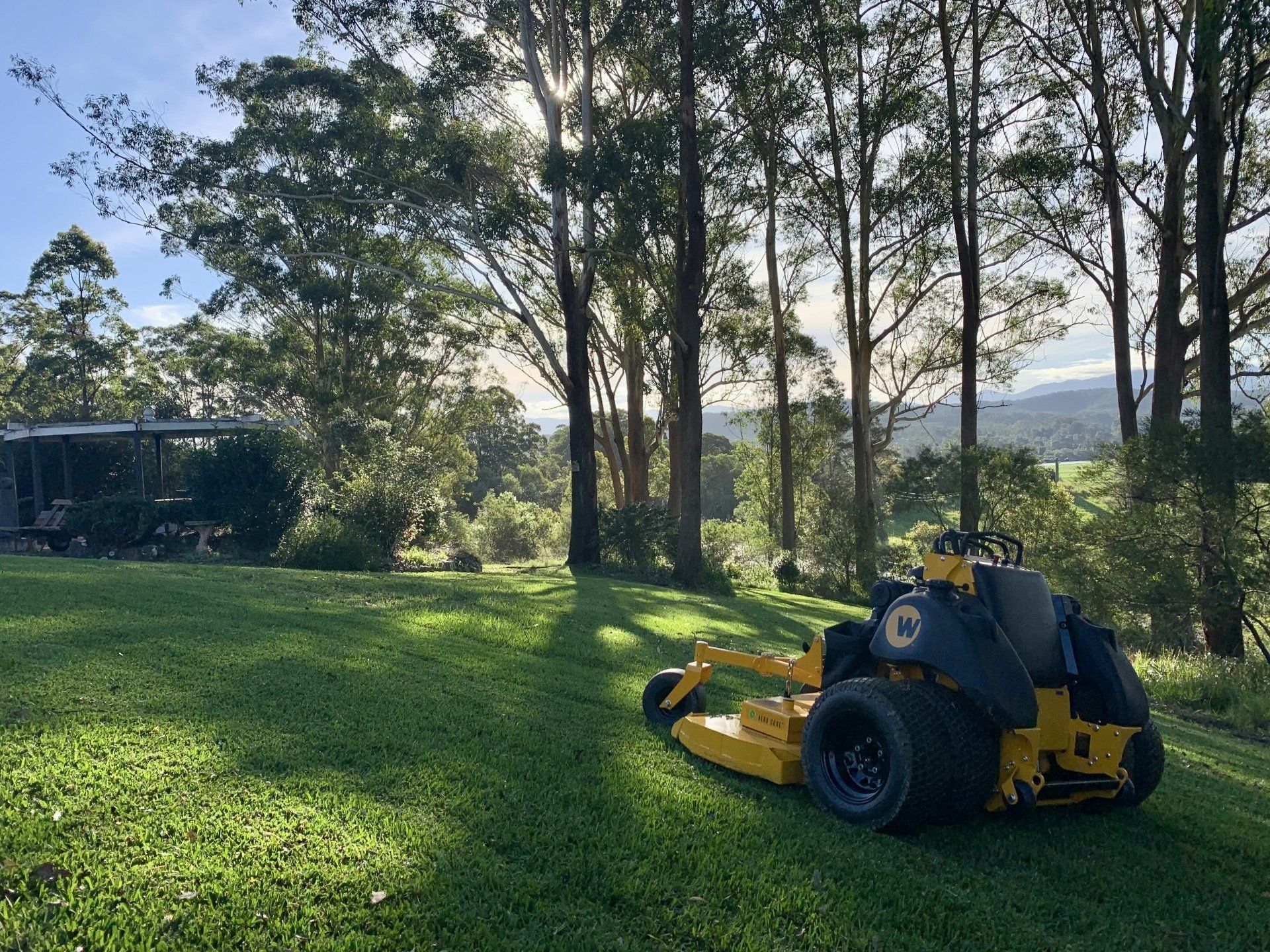 A Yellow Lawn Mower Is Parked in The Middle of A Lush Green Field — All Round Ground Maintenance in Woolgoolga, NSW