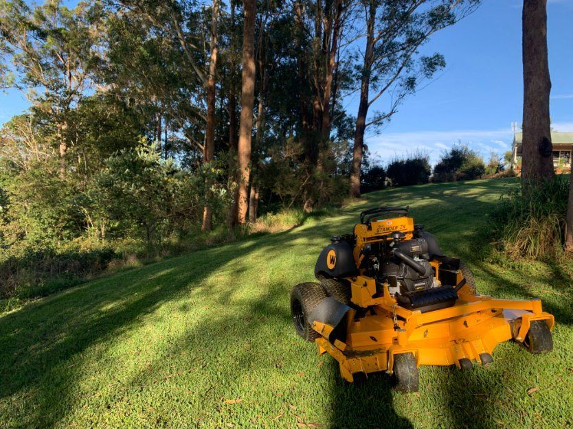 A Yellow Lawn Mower Is Sitting on Top of A Lush Green Lawn — All Round Ground Maintenance in Woolgoolga, NSW