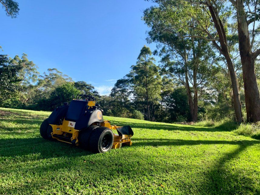 A Yellow Lawn Mower Is Sitting on Top of A Lush Green Field — All Round Ground Maintenance in Nana Glen, NSW